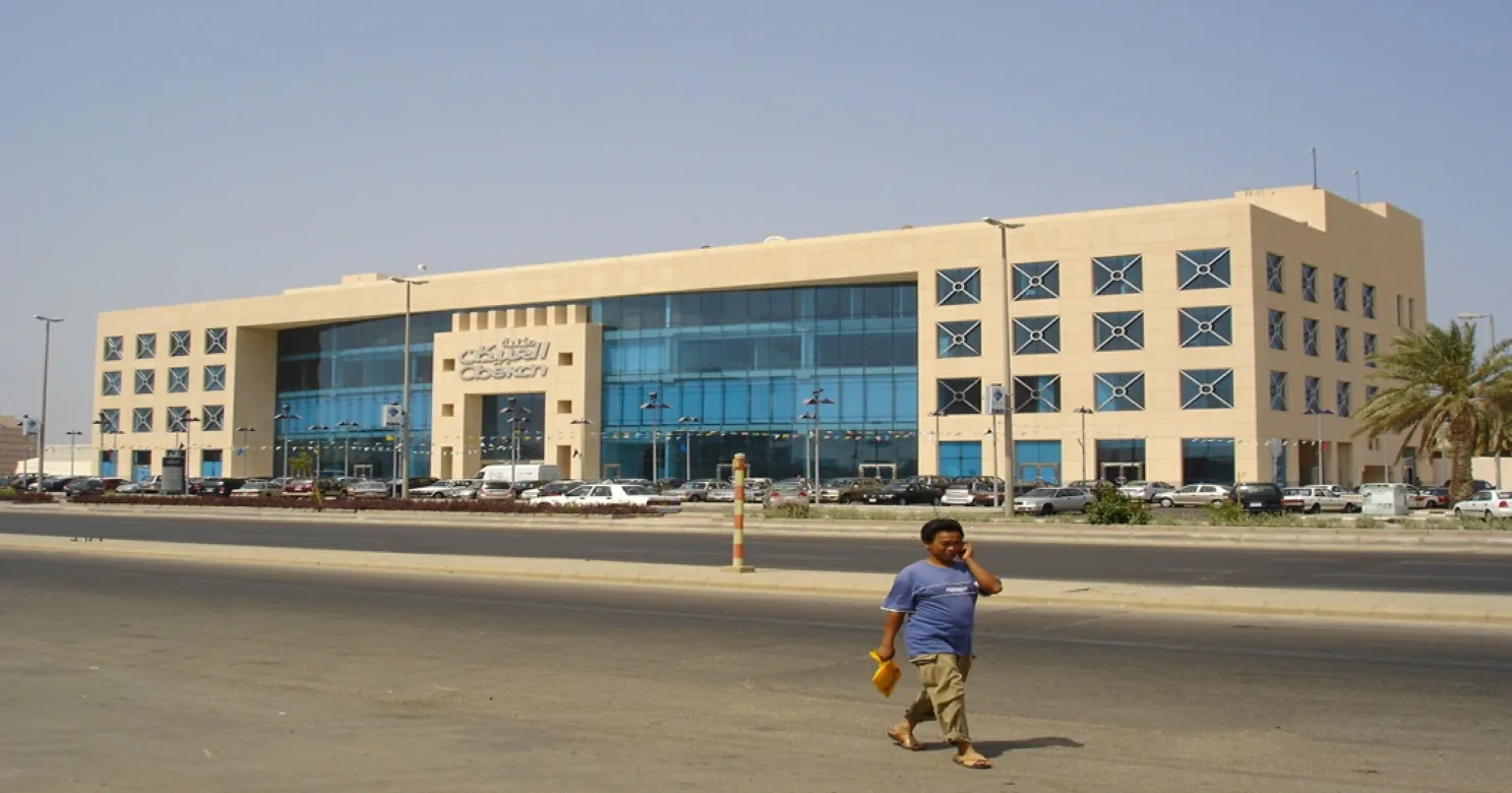 Sand-coloured multi-storey building with a blue glass centre bay and patterned square windows, seen across a road and car park