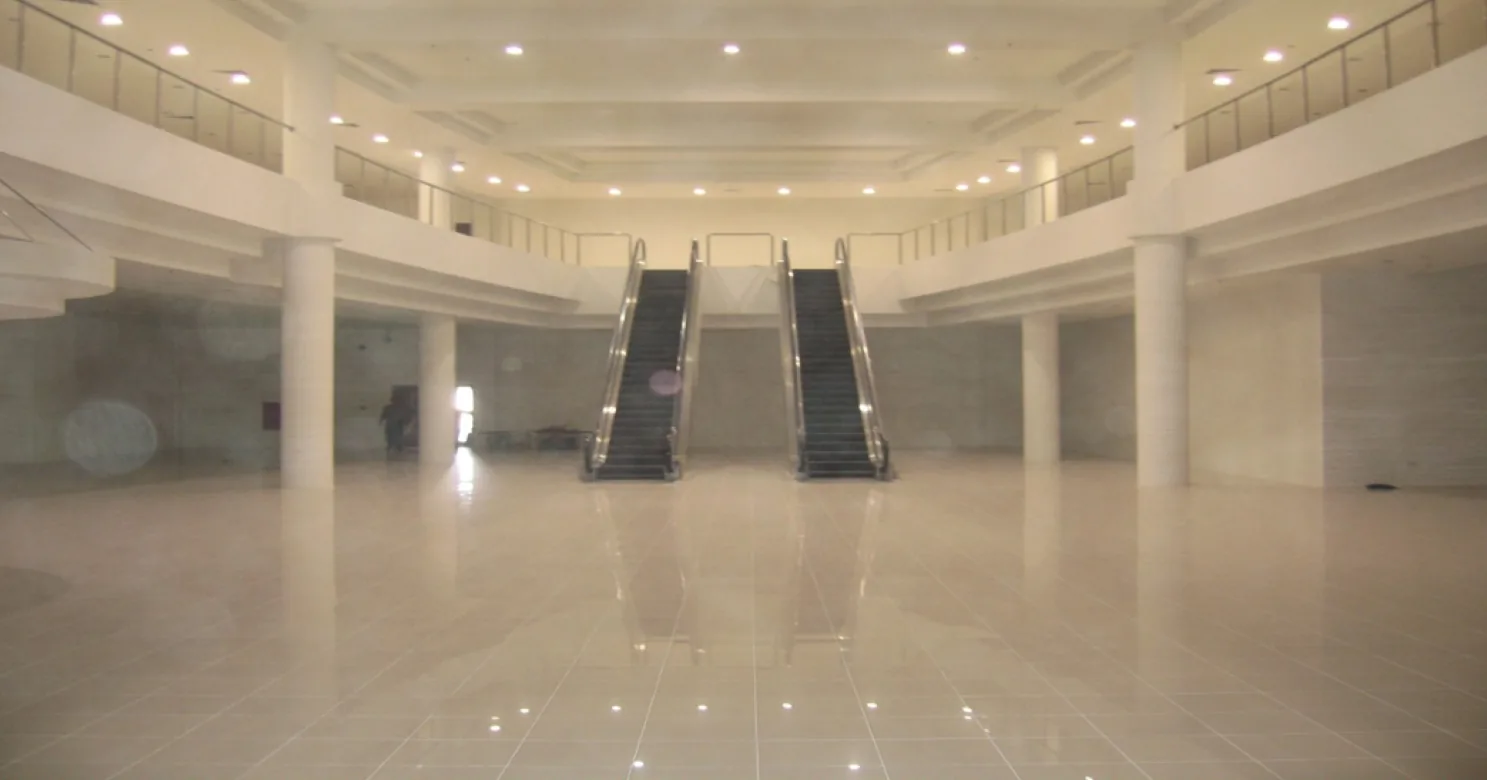 Double-height atrium with twin escalators to balustraded upper galleries, recessed downlights and a wide polished cream tile floor