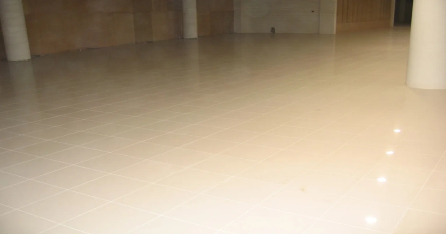 Wide expanse of polished cream floor tile with small downlight reflections, white columns and timber-toned boarding along the far wall