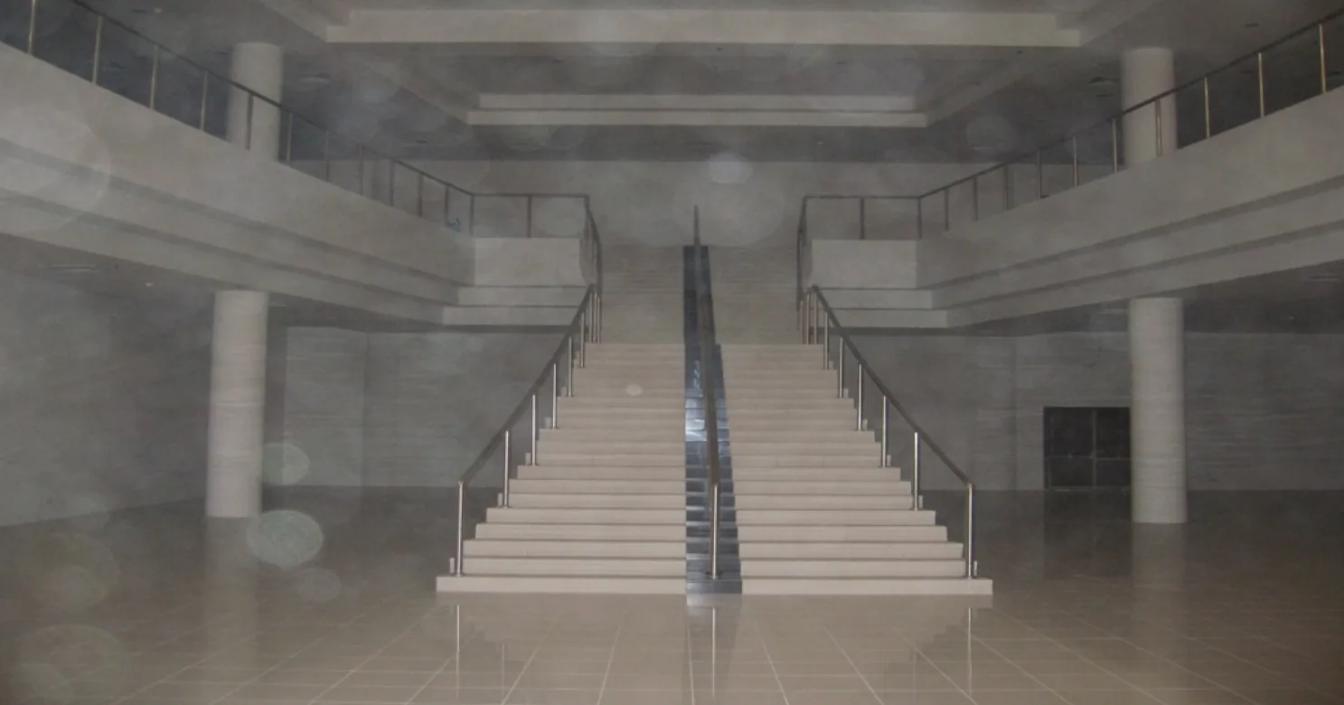 Symmetrical double staircase with a dark central divider and steel handrails rising toward balconies on both sides, in a hazy hall