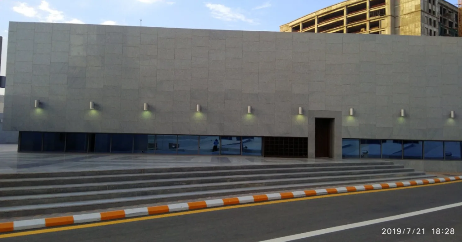 Grey stone-clad wall with a row of cylindrical wall lights above broad steps, and an orange-and-white kerb beside the road.