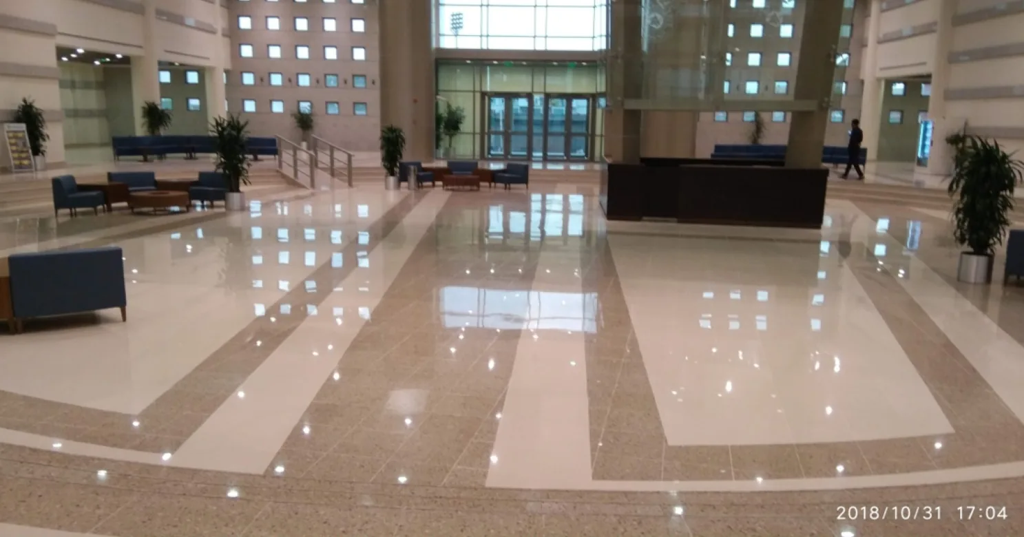 Finished lobby with a polished floor in cream and tan bands, blue sofas, a dark reception desk, plants and a man walking.