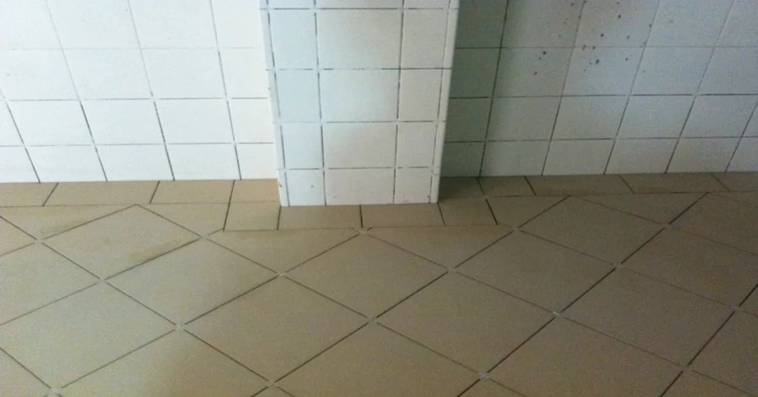 White wall tiles meeting diagonally laid tan floor tiles at a column base, with even grout lines.