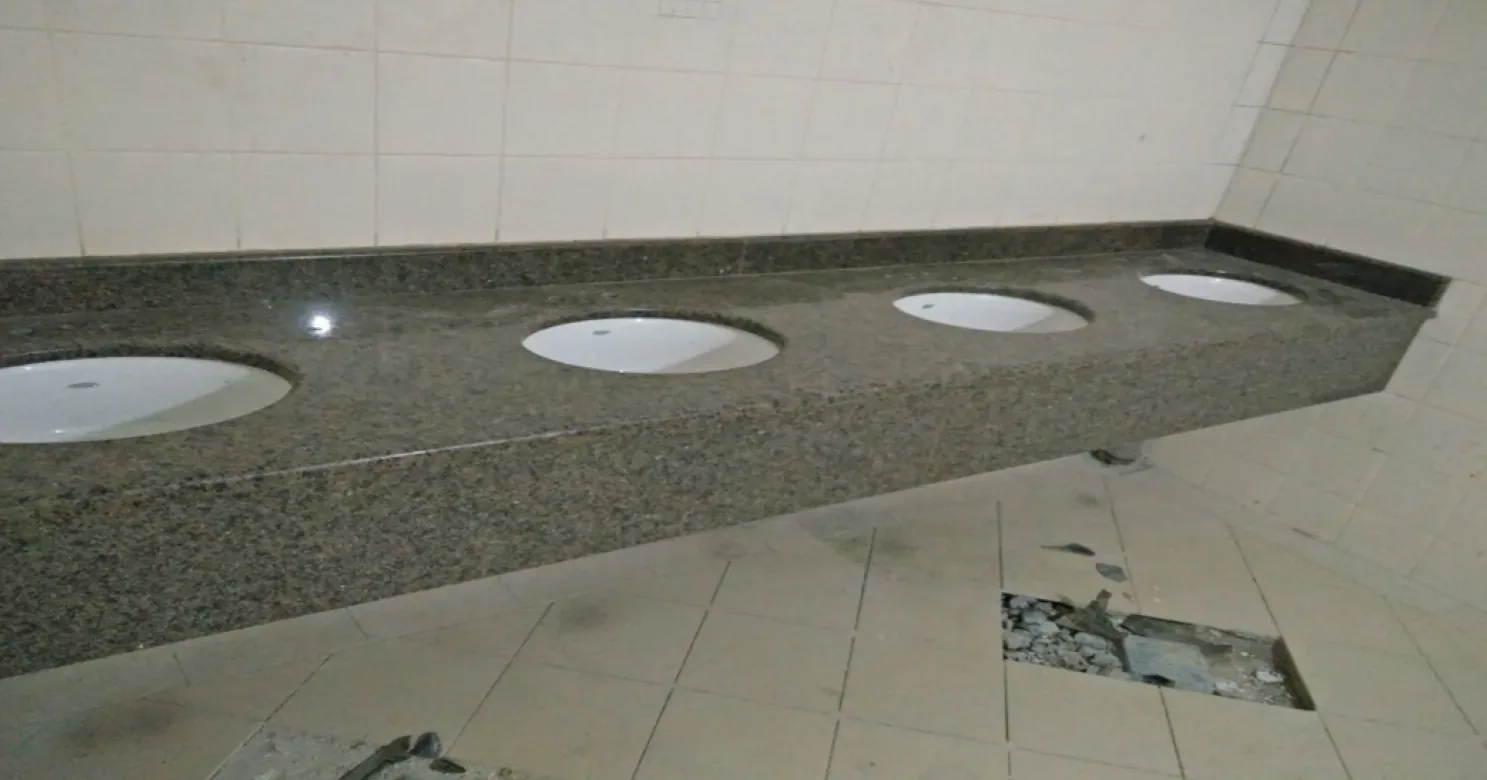 Angled close view of a granite counter with four inset basins, beside a missing floor-tile section exposing rubble.