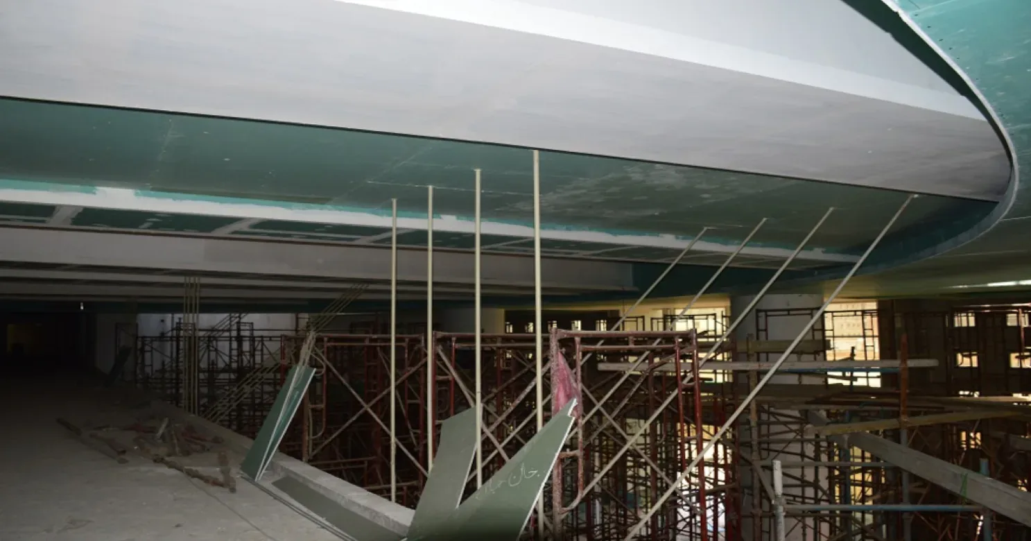 Large curved plasterboard bulkhead under construction over scaffolding, with hanger rods and green board offcuts leaning on the floor.