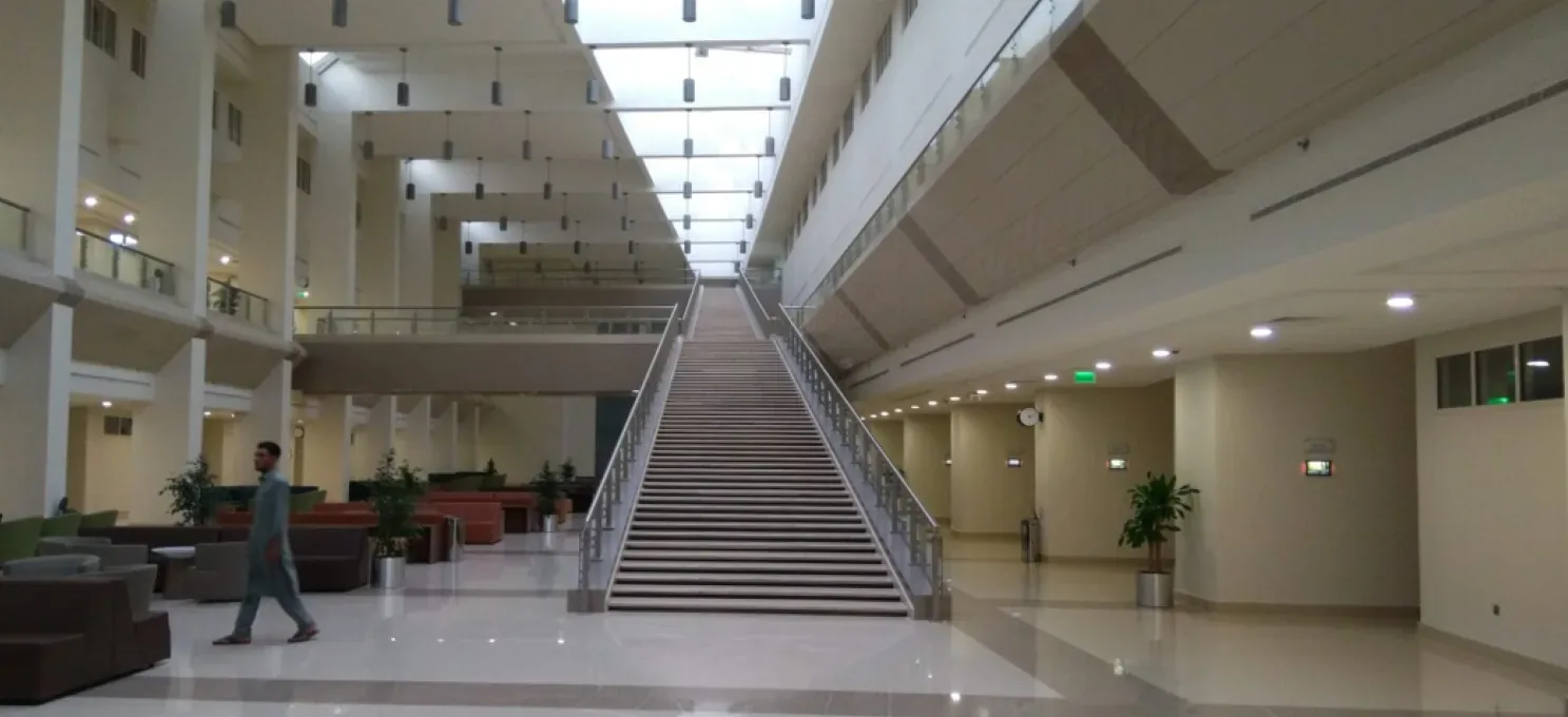 Finished atrium with a long central staircase between steel-and-glass railings, upper galleries, sofas and a man walking at left.