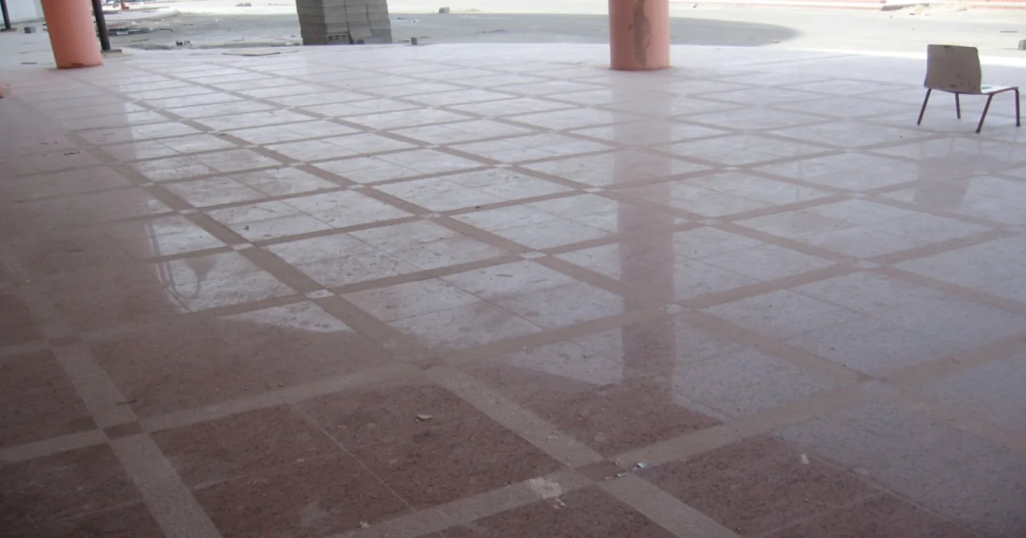 Polished reddish speckled stone-effect floor on a diagonal grid of pale border strips, with pink columns and a lone chair