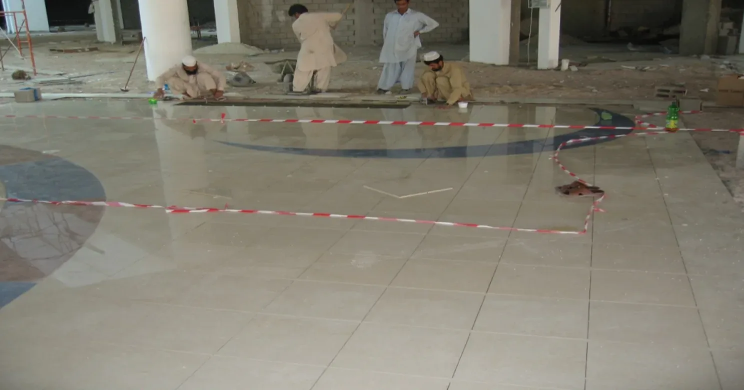 Four workers at the far side of a polished cream tile floor marked off with tape, a dark blue medallion arc inlaid