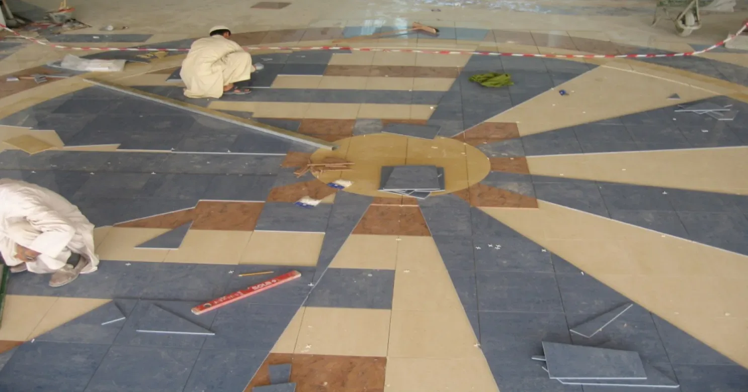 Blue, terracotta and tan tile segments dry-laid in a star around a circular yellow hub, with two installers and a spirit level