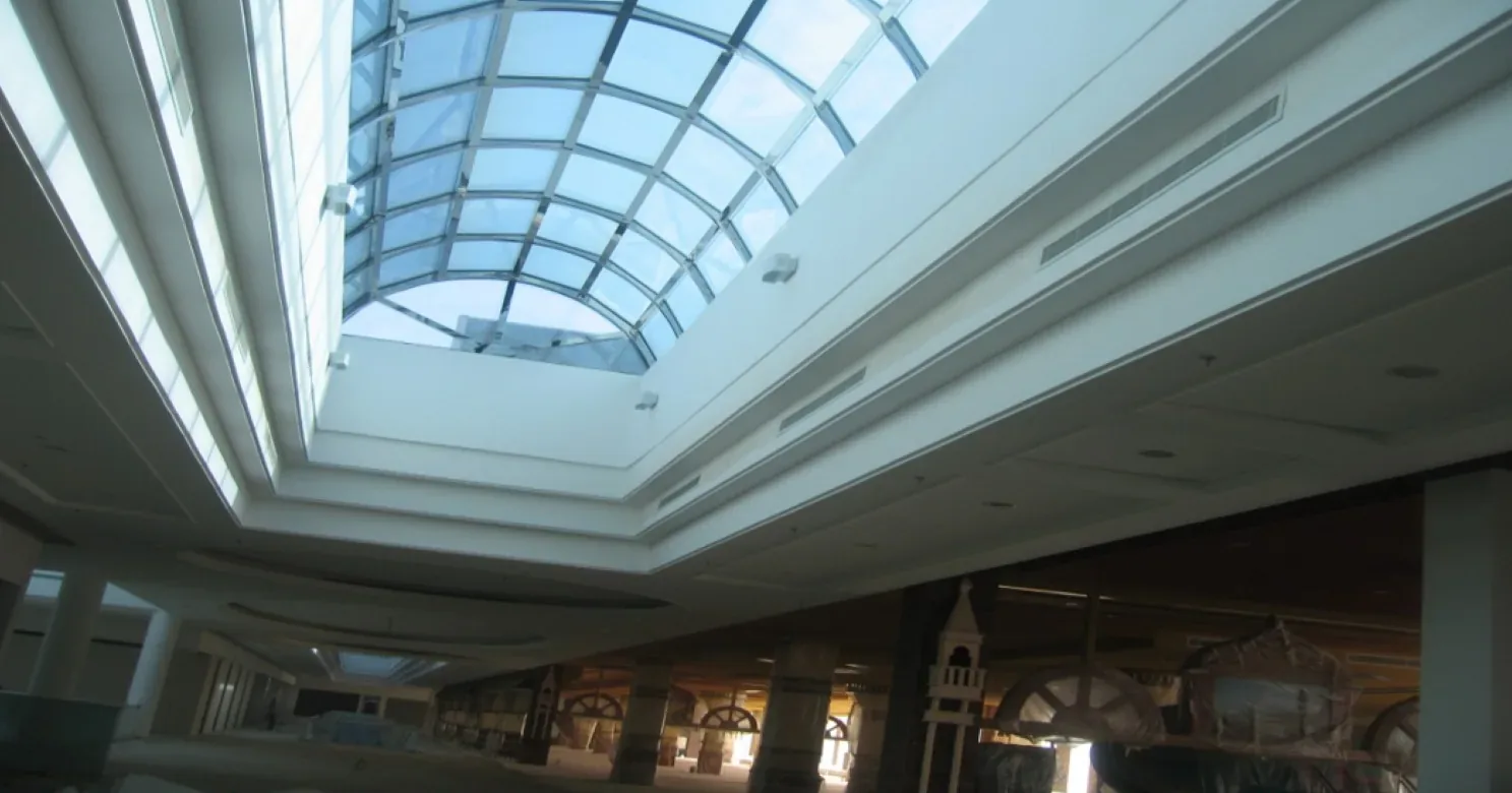 Looking up at an arched glass skylight framed by a white stepped ceiling, with decorative props in the dim space below