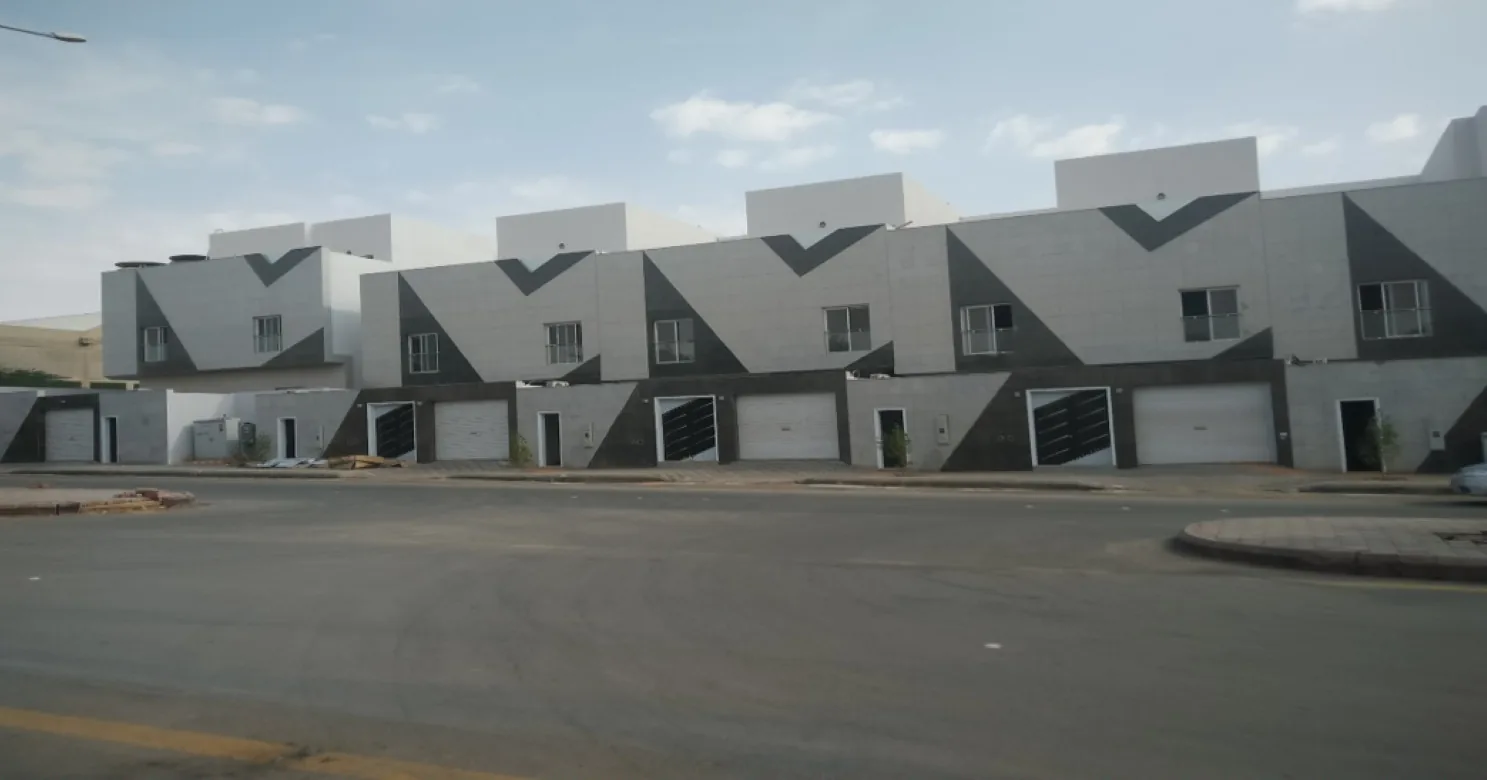 Finished row of two-storey townhouses on a street, grey facades with dark triangular accents and roller garage doors, empty road in front.