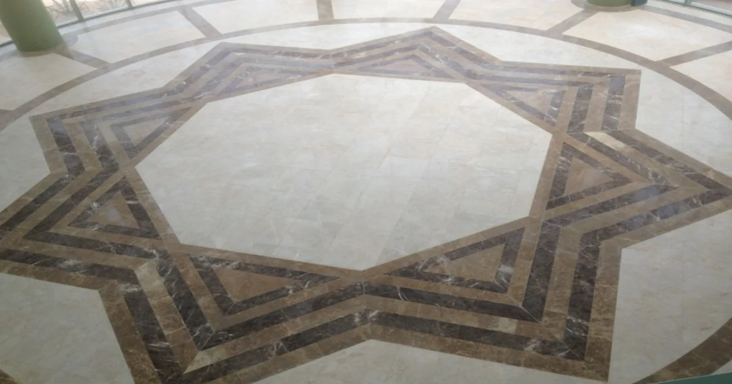Eight-point star inlay in brown and dark-veined marble set into a cream marble floor, with a green column at top left.