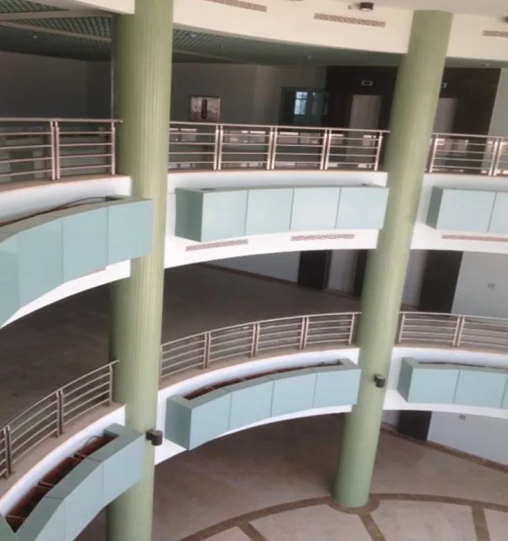 Two green fluted columns frame curved atrium balconies with steel-bar railings and pale-green edge panels, viewed from above.