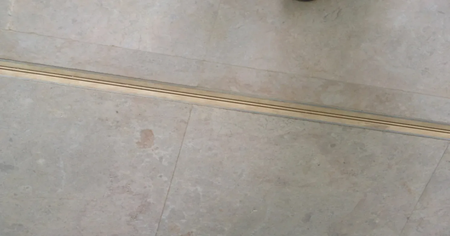 Close-up of grey-beige stone floor tiles with a brass-coloured metal strip set into the joint between two areas.