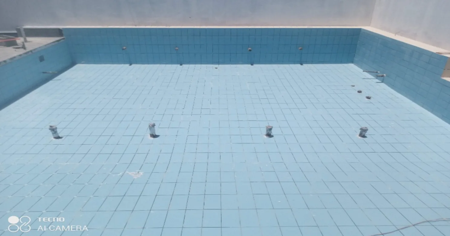 Empty blue-tiled pool shell with pipe fittings projecting from its floor and walls.