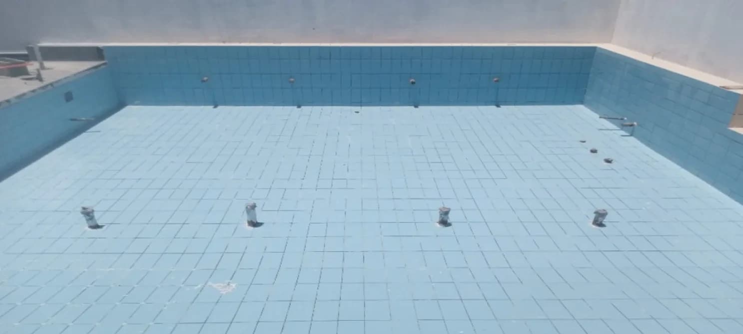 Blue square tiles line the floor and walls of an empty pool, with fittings set in the floor and back wall.