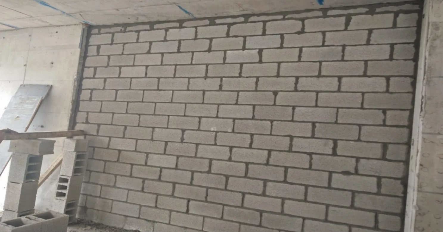 Close view of a concrete-block wall with raw mortar joints, hollow blocks stacked at left and bare concrete walls beside it.