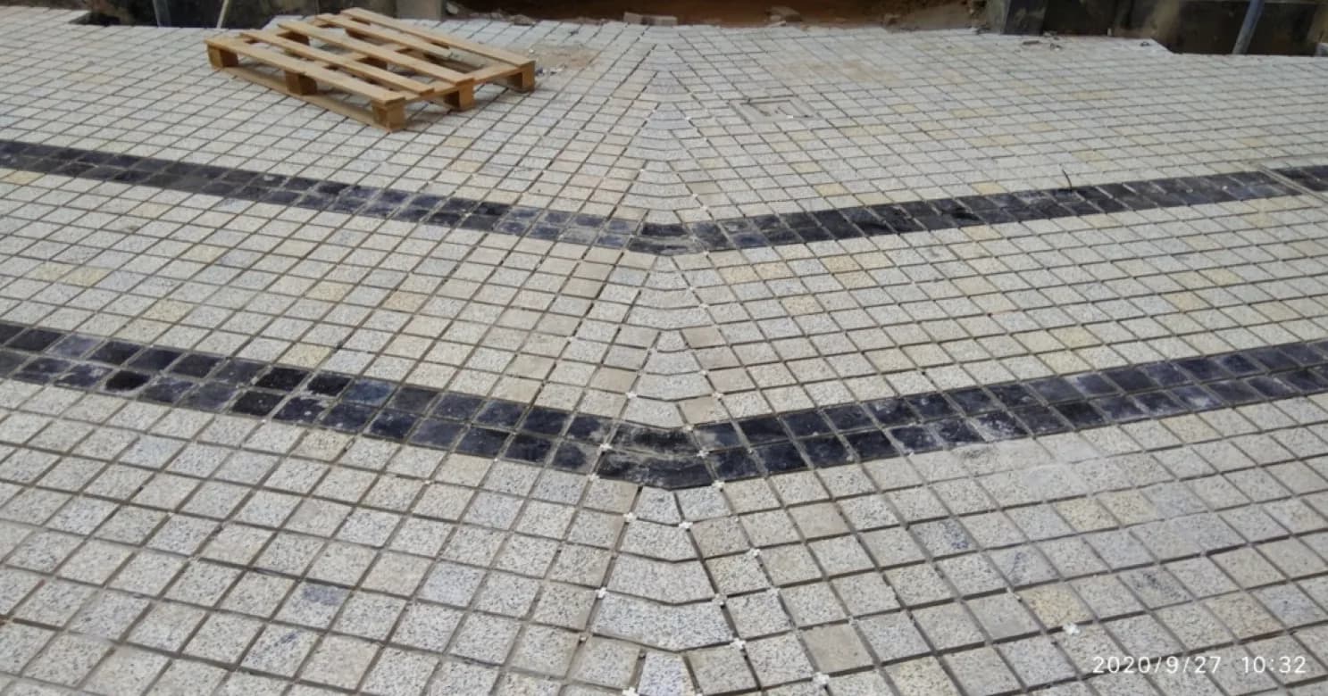 Small granite mosaic pieces set with spacers in a mitred layout, dark inlay bands meeting at an angle, and a wooden pallet.