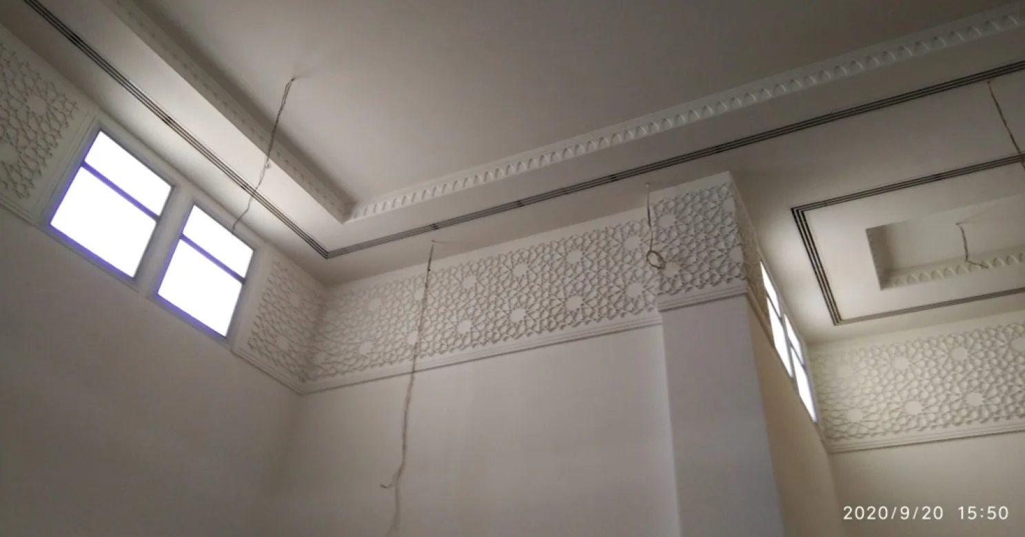 Interior corner with a dentil cornice, a band of geometric relief pattern near the ceiling, dangling wires and overexposed windows.