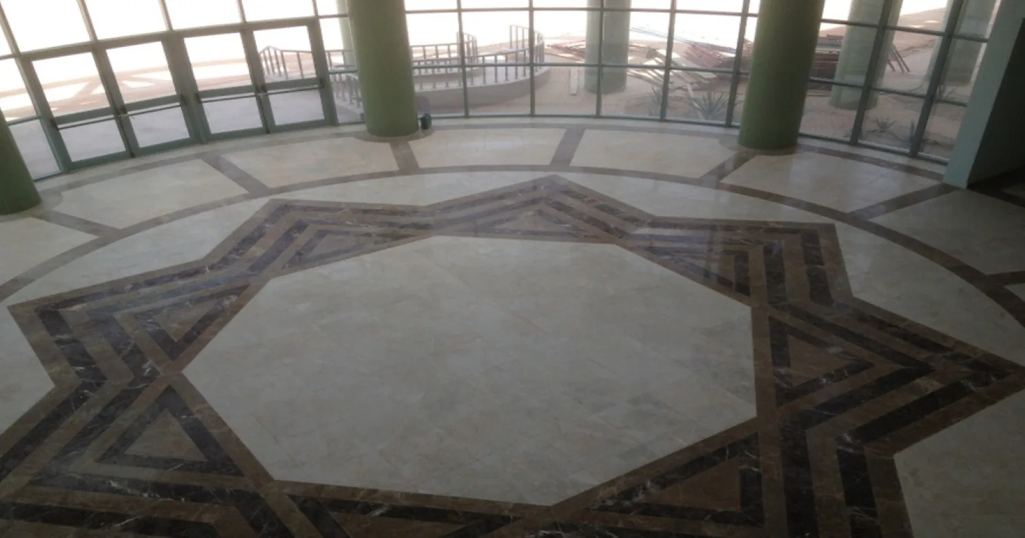 Polished cream marble floor with an eight-pointed star inlay in brown and dark marble, beside a curved glazed wall and green columns.