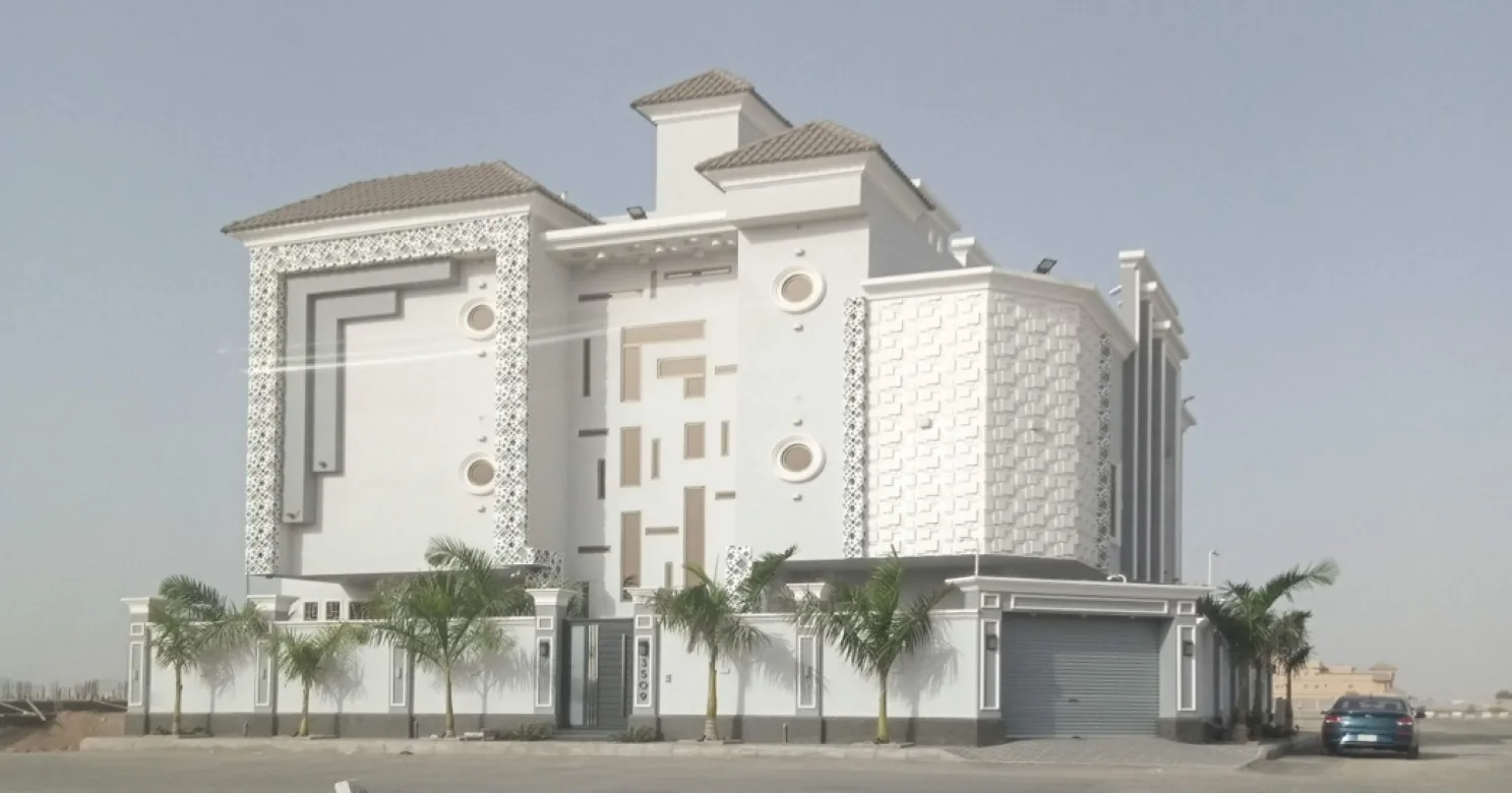 Multi-storey white villa with a lattice-patterned facade border, round windows, a textured block-relief bay, palms and a garage shutter.