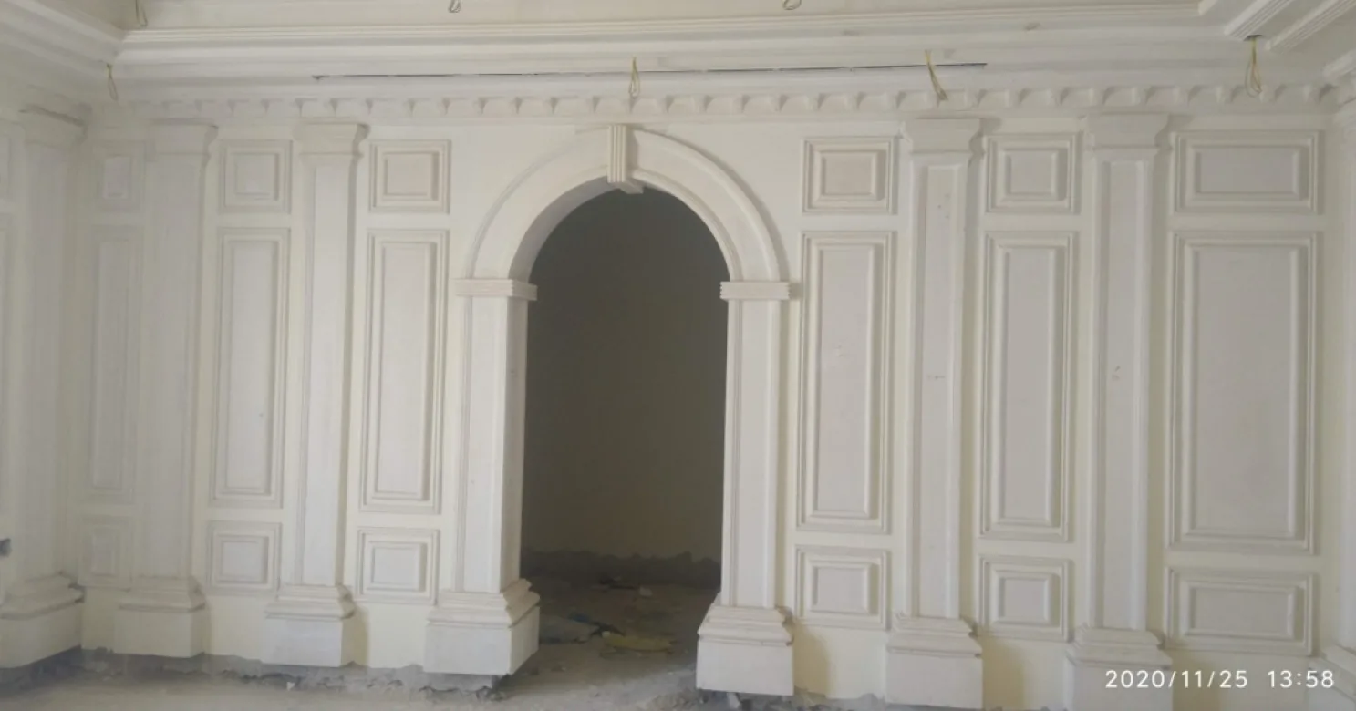 Unpainted white classical gypsum wall with an arched opening, pilasters, panel mouldings and a dentil cornice.