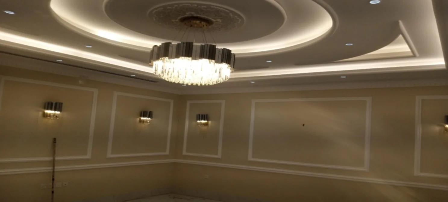 Cream-walled room with a curved cove-lit tiered ceiling, central rosette, crystal chandelier, moulded wall panels and wall lights.