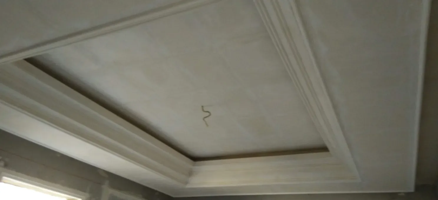 Unpainted gypsum tray ceiling with a stepped cornice and a cable stub at the centre, above bare walls.