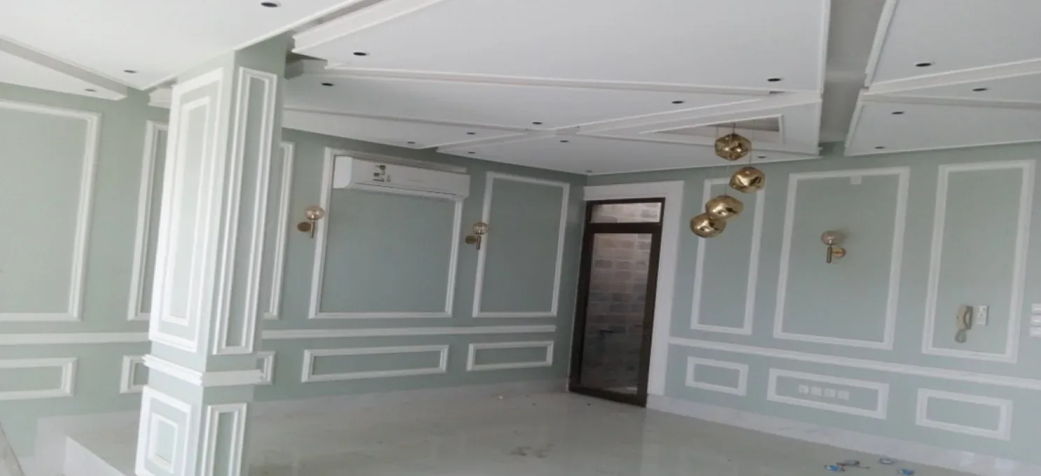Bright hall with pale-green walls framed by white mouldings, a stepped gypsum ceiling with downlights, gold pendants and a polished marble-look floor.