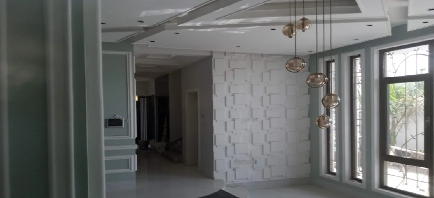 Interior with a white textured block-relief feature wall, amber glass pendant lights, tall aluminium windows and a stepped ceiling with downlights.