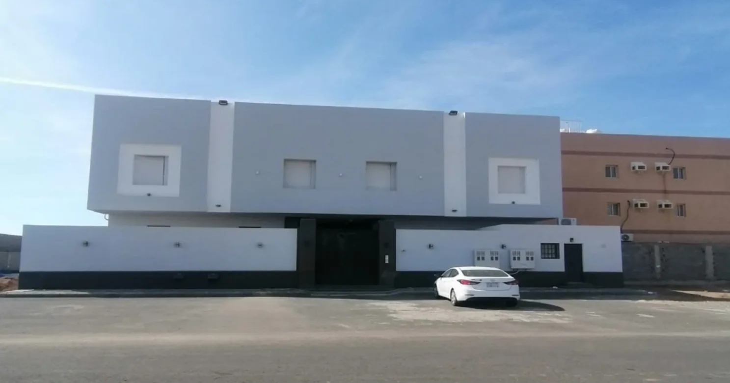 Two-storey villa with a grey and white facade, square window surrounds, dark base band and boundary wall, and a white car outside.