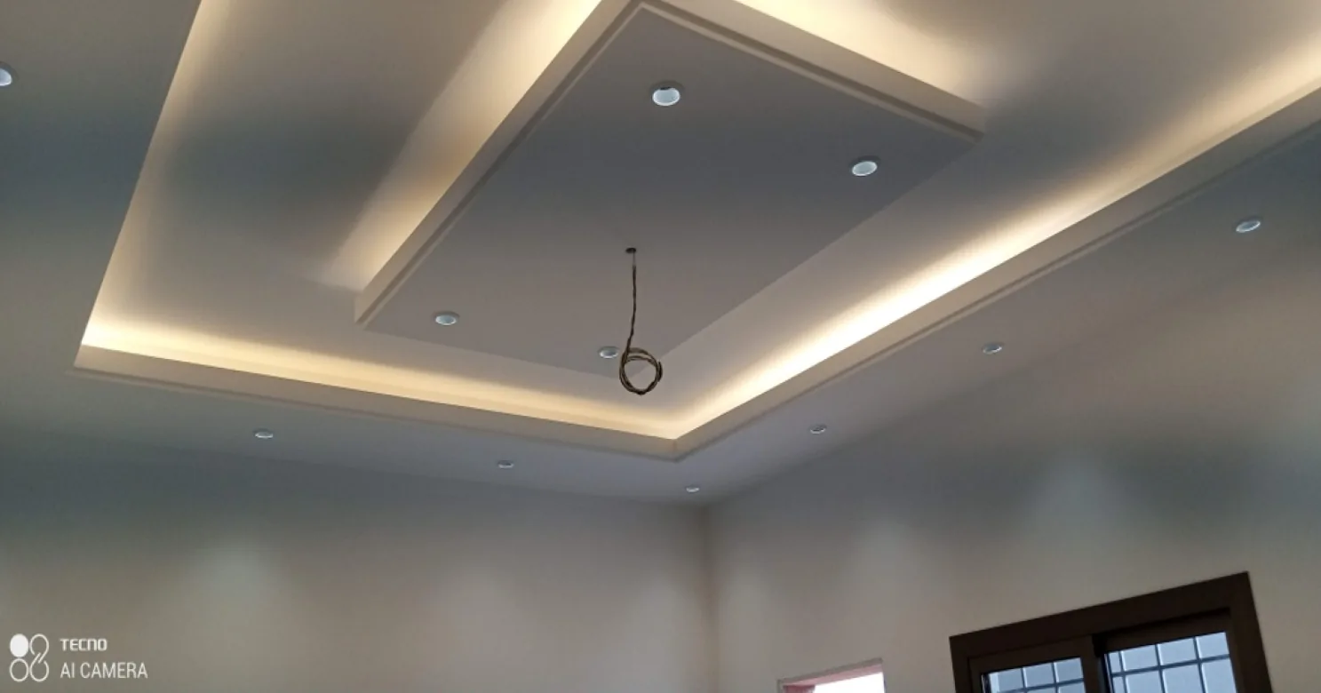 Stepped cove-lit tray ceiling with recessed downlights and a pendant cable hanging from the centre.