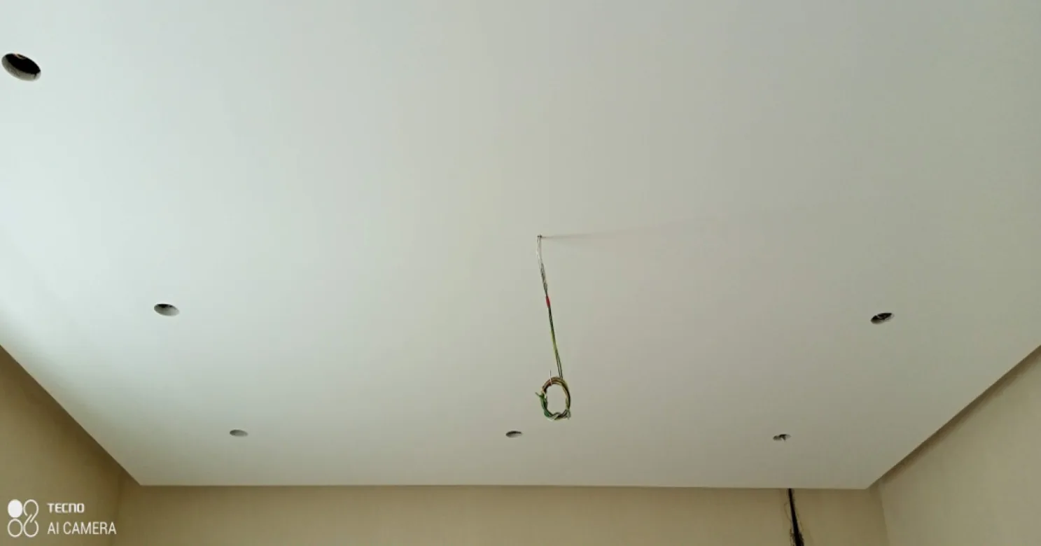 Flat white ceiling with downlight openings and a cable hanging from its centre, above cream walls.