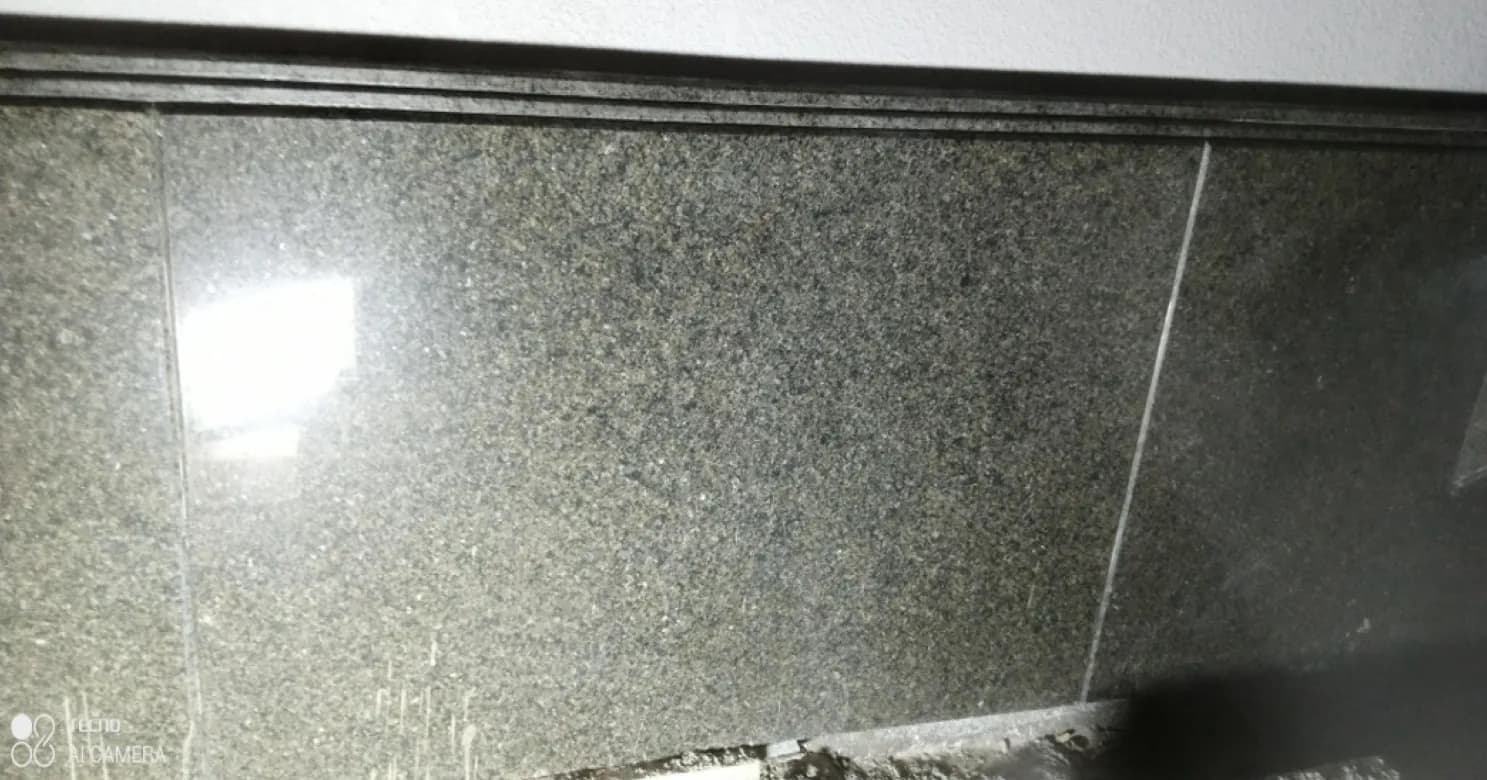 Close-up of polished dark granite wall slabs with a stepped moulding along the top edge and a bright reflection on the left.