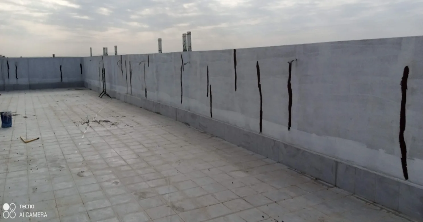 Roof terrace with a tiled floor and a grey parapet wall marked by vertical black bituminous strips, vent pipes rising above it.