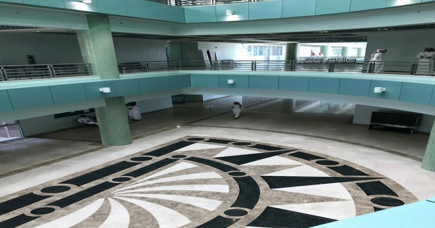 Atrium from an upper gallery, with a circular marble inlay in cream and black, teal-faced balconies, steel railings and a few people.
