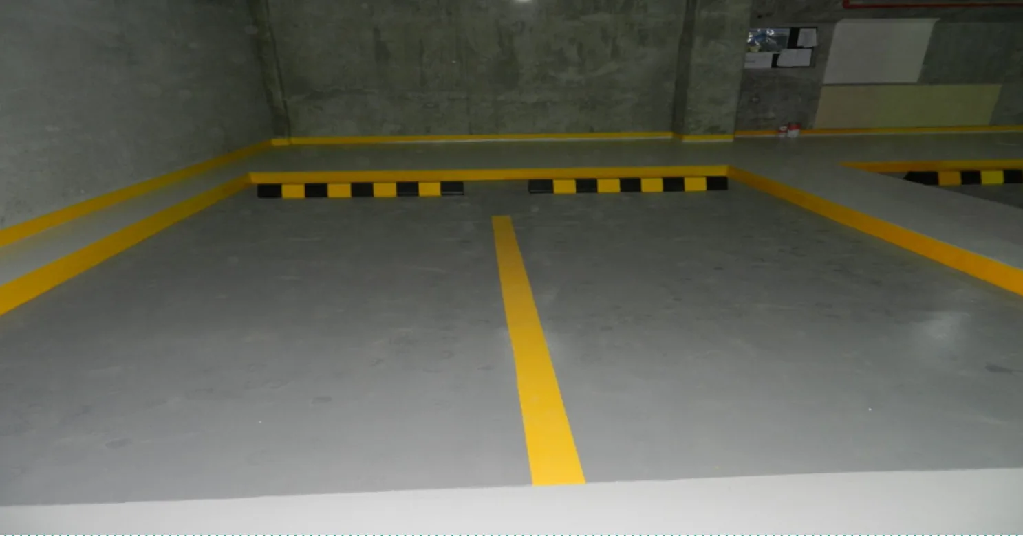 Basement parking bay with a grey finished floor, yellow marking lines and black-and-yellow wheel stops; no vehicles present.