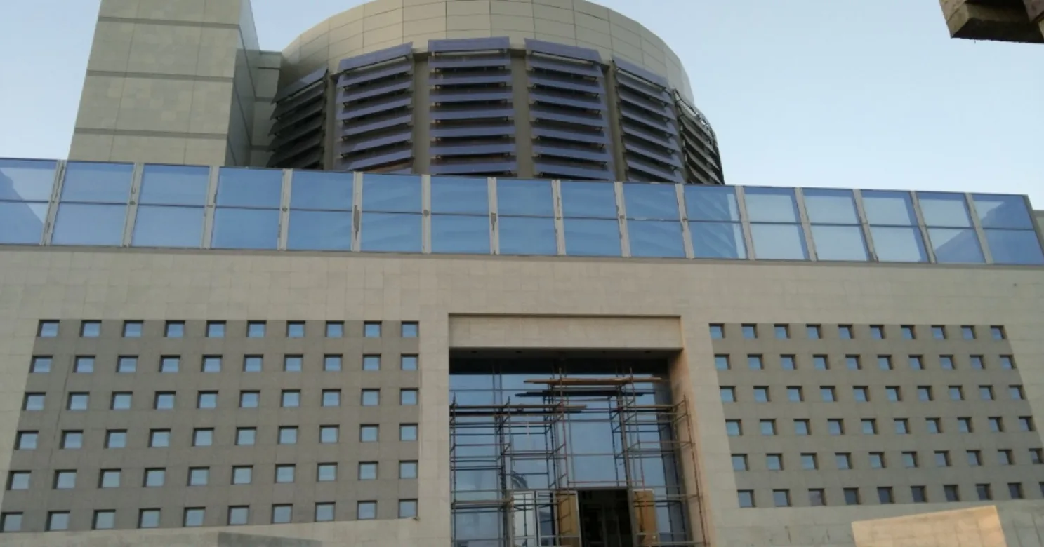 Close view of the entrance: stone cladding with a square window grid, blue glass band, louvred round top and scaffolded glazing.