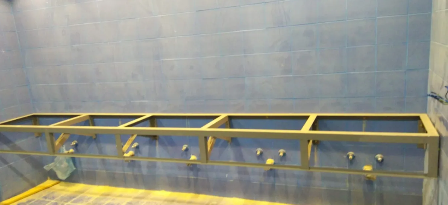 Steel frame for a basin counter fixed to a blue-tiled wall, with five sets of supply and drain stubs projecting below it.