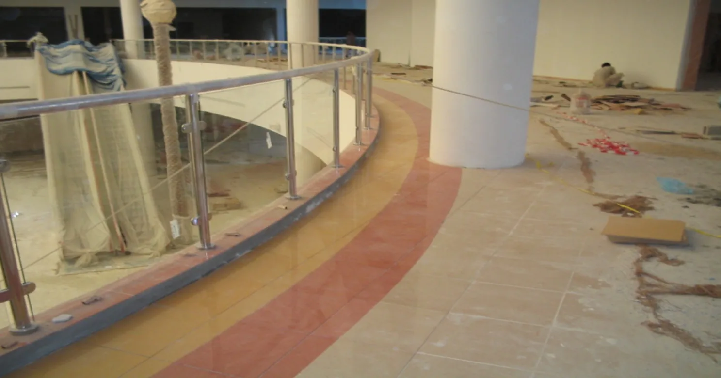 Curved ochre and terracotta bands sweeping along a stainless-steel and glass balustrade past a white column on a polished floor