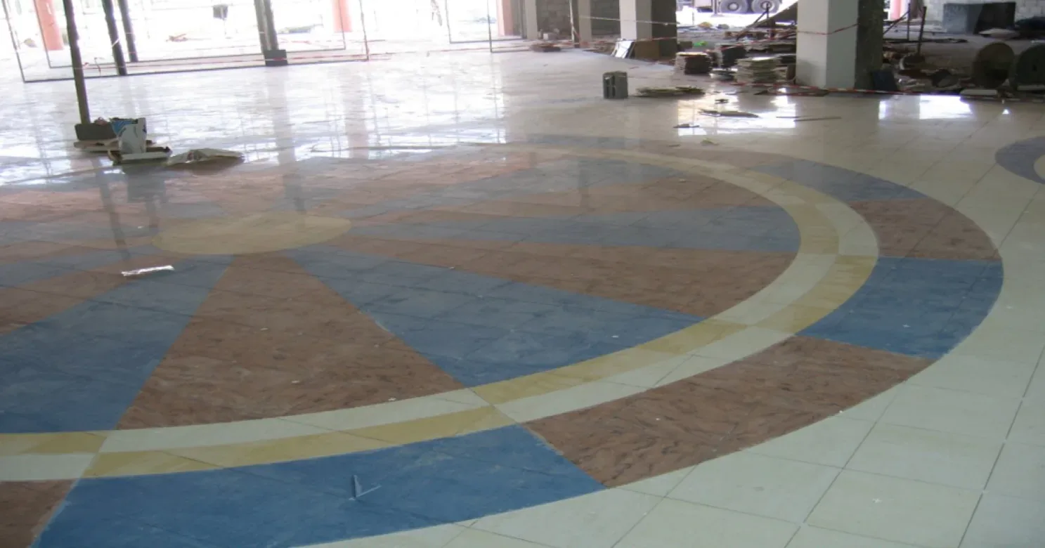 Radiating blue and terracotta wedges within concentric cream and yellow rings form a large floor medallion set in polished cream tile