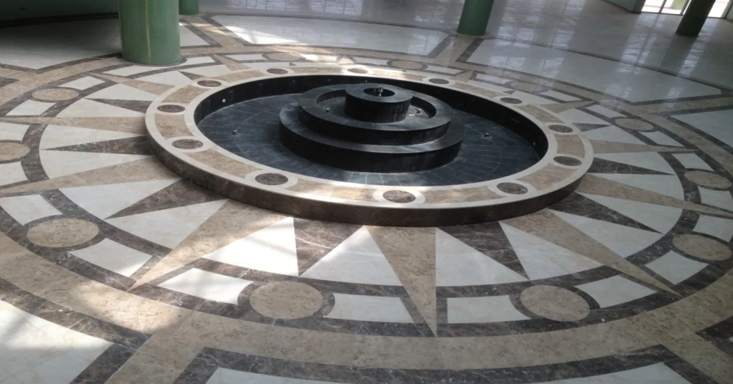 Finished tiered black stone fountain at the centre of a compass-rose marble floor in brown, cream and dark marble.