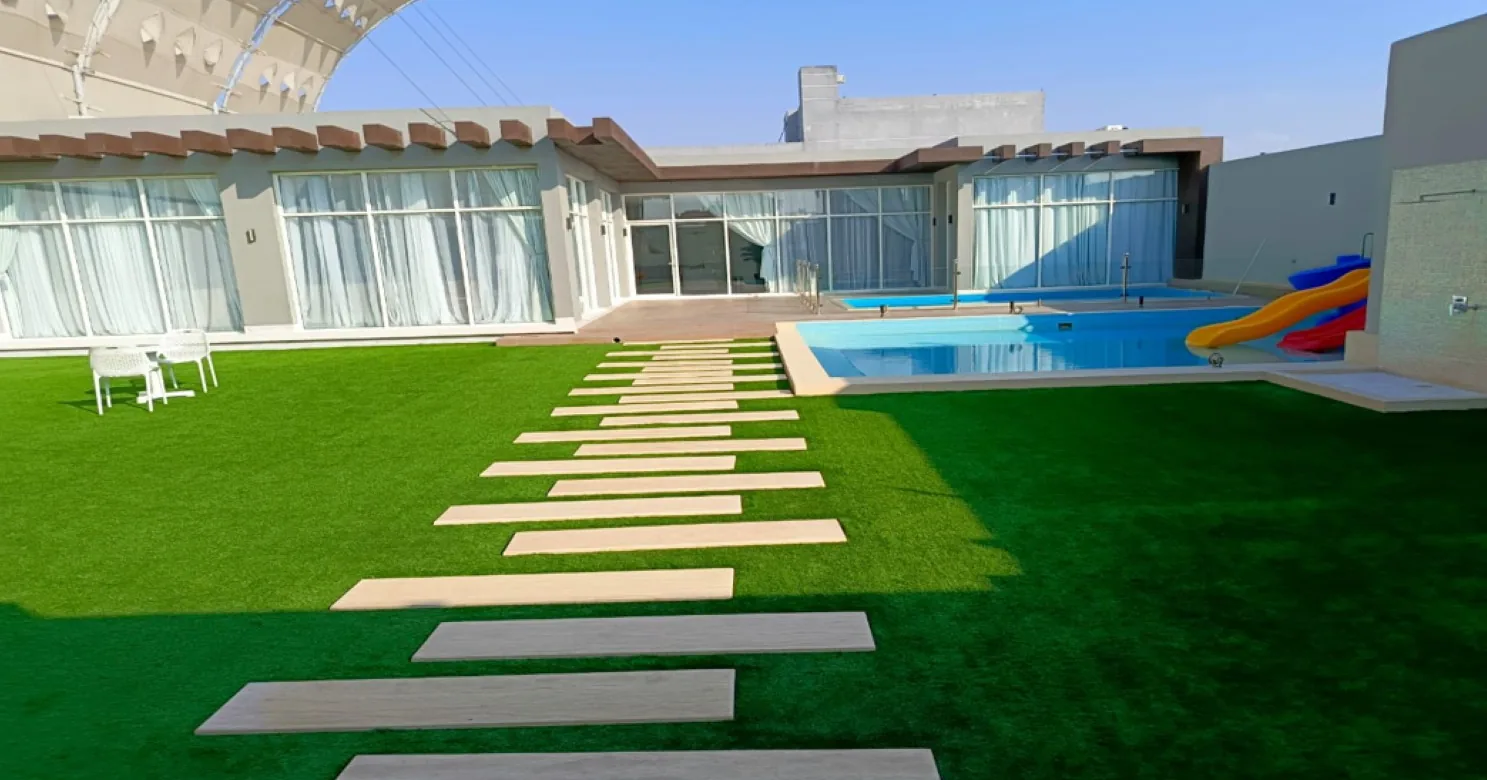 Garden with green turf, a stepping-slab path, a pool with a slide and a glass-fronted pavilion; canopy just visible at top left.