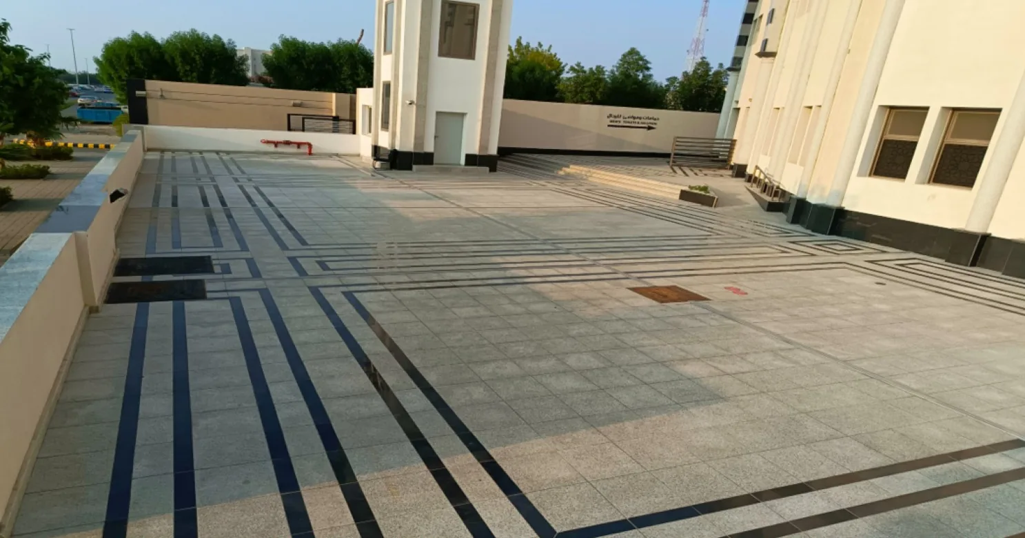 Completed granite courtyard in large slabs with black and navy inlay lines, a manhole cover and low walls beside a white building.