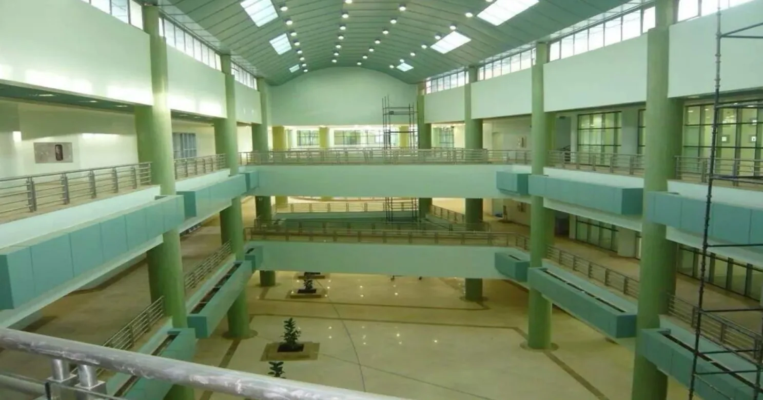 Multi-storey atrium under a barrel-vaulted skylit roof, with green columns, teal-faced galleries, steel railings and scaffold towers still standing.
