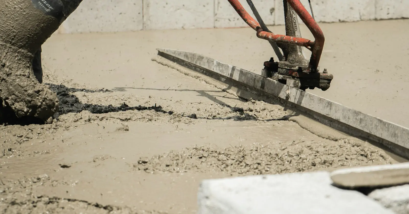 A worker using a petrol-driven power screed to level freshly placed concrete