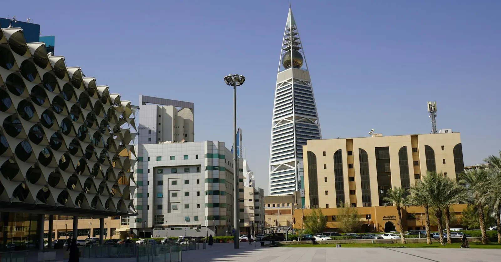 Central Riyadh: a tall pointed tower rising above mid-rise buildings and palm trees, with a lattice-fronted building at left