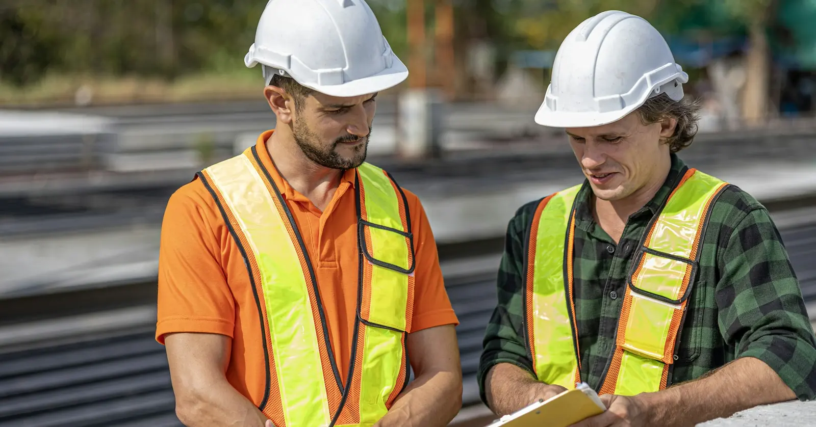 Two site staff in hard hats and high-visibility vests reviewing notes on a clipboard