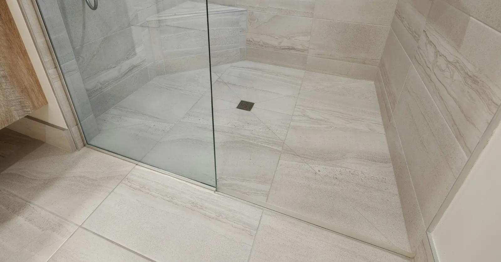 Tiled walk-in shower area behind a glass screen, with the floor falling to a small drain